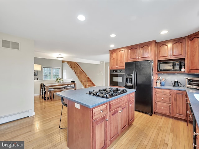 kitchen with baseboard heating, light wood-style flooring, a center island, visible vents, and black appliances