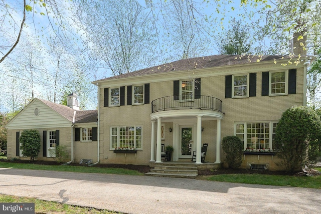 view of front facade with a chimney, brick siding, and a balcony