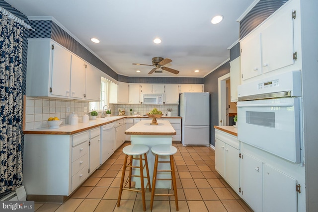 kitchen with white appliances, crown molding, ceiling fan, light countertops, and white cabinets