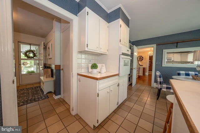 kitchen with wallpapered walls, light tile patterned flooring, white oven, light countertops, and white cabinets