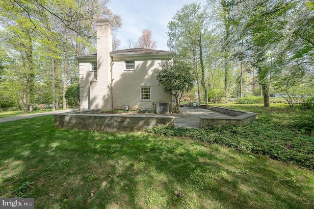 rear view of house with a lawn, cooling unit, a patio area, and a chimney