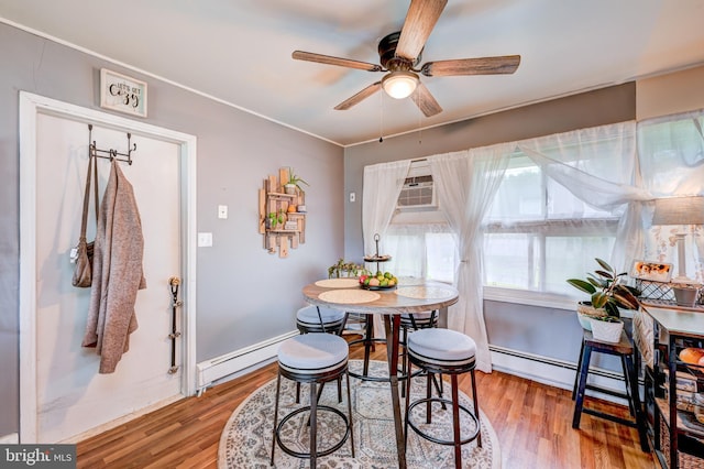 dining space with baseboards, wood finished floors, a ceiling fan, and a baseboard heating unit