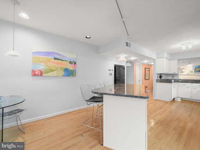 kitchen featuring freestanding refrigerator, light wood-type flooring, white cabinetry, a breakfast bar, and baseboards