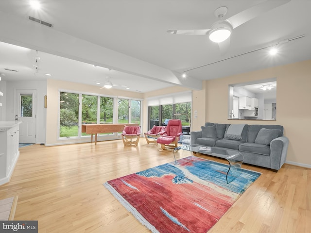 living area featuring a ceiling fan, light wood finished floors, baseboards, and rail lighting