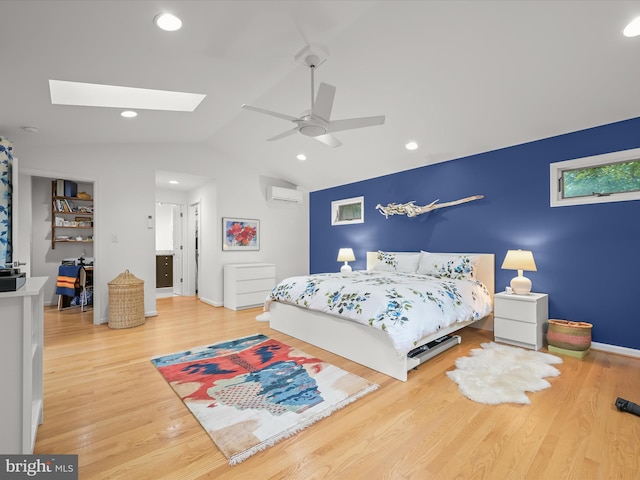 bedroom with an AC wall unit, lofted ceiling, a skylight, wood finished floors, and ceiling fan