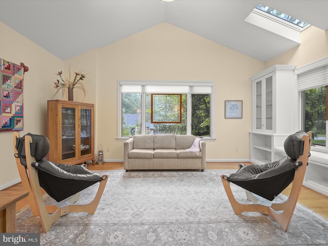 living area featuring a skylight, lofted ceiling, light wood finished floors, and baseboards