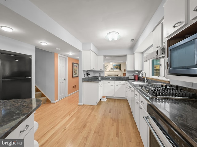 kitchen with appliances with stainless steel finishes, light wood finished floors, white cabinetry, and a sink