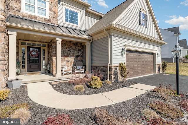 property entrance with driveway, a standing seam roof, covered porch, a garage, and stone siding