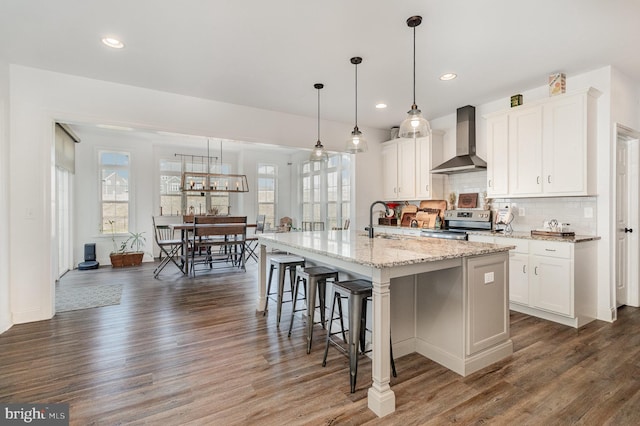 kitchen with a breakfast bar area, wall chimney exhaust hood, stainless steel electric range, dark wood-type flooring, and decorative backsplash