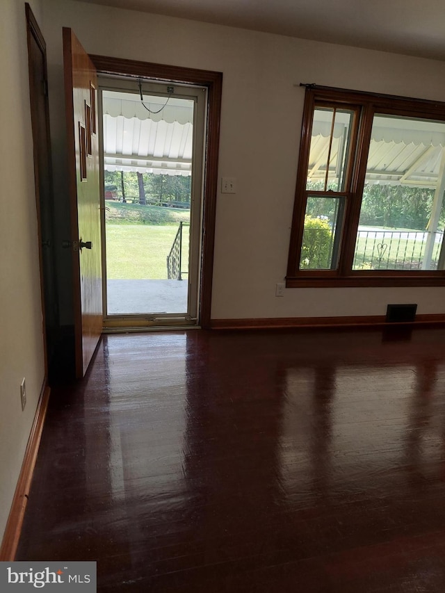 unfurnished room featuring baseboards, wood finished floors, and a wealth of natural light