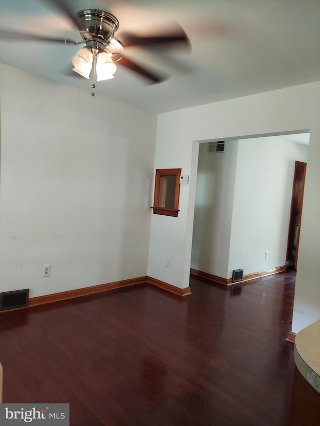 empty room with visible vents, a ceiling fan, and dark wood finished floors