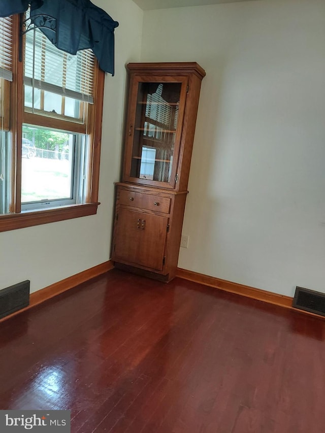 empty room featuring baseboards, dark wood finished floors, and visible vents
