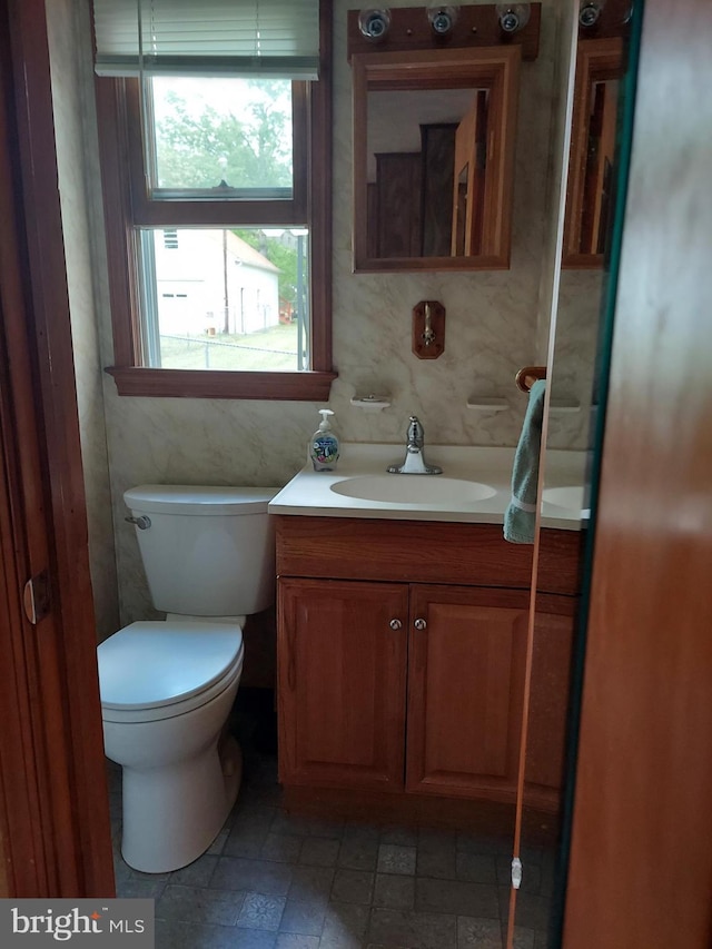 half bath with vanity, stone finish floor, and toilet