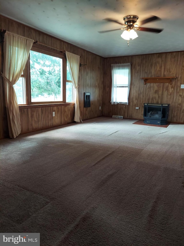 unfurnished living room featuring carpet floors, ceiling fan, and wood walls