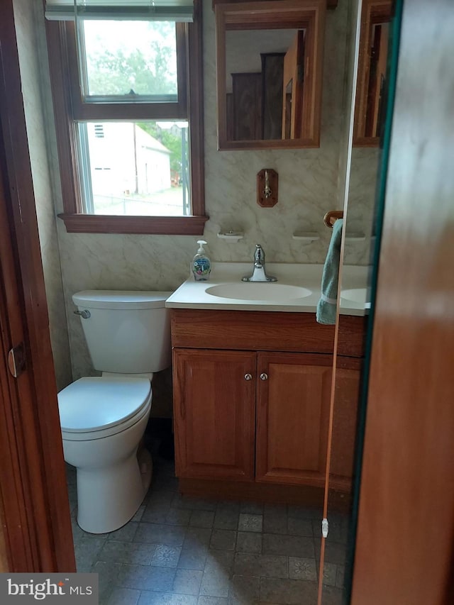 half bath with vanity, stone finish flooring, a wealth of natural light, and toilet