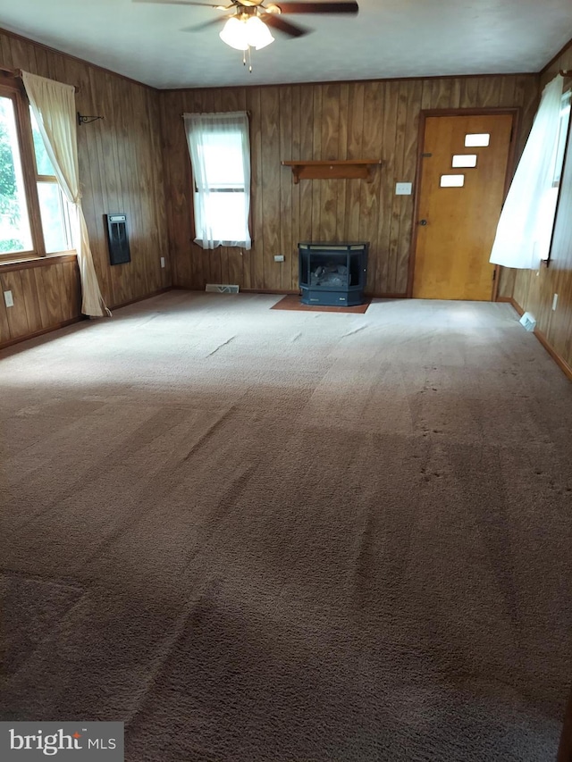unfurnished living room featuring carpet floors, a wood stove, a ceiling fan, and wood walls