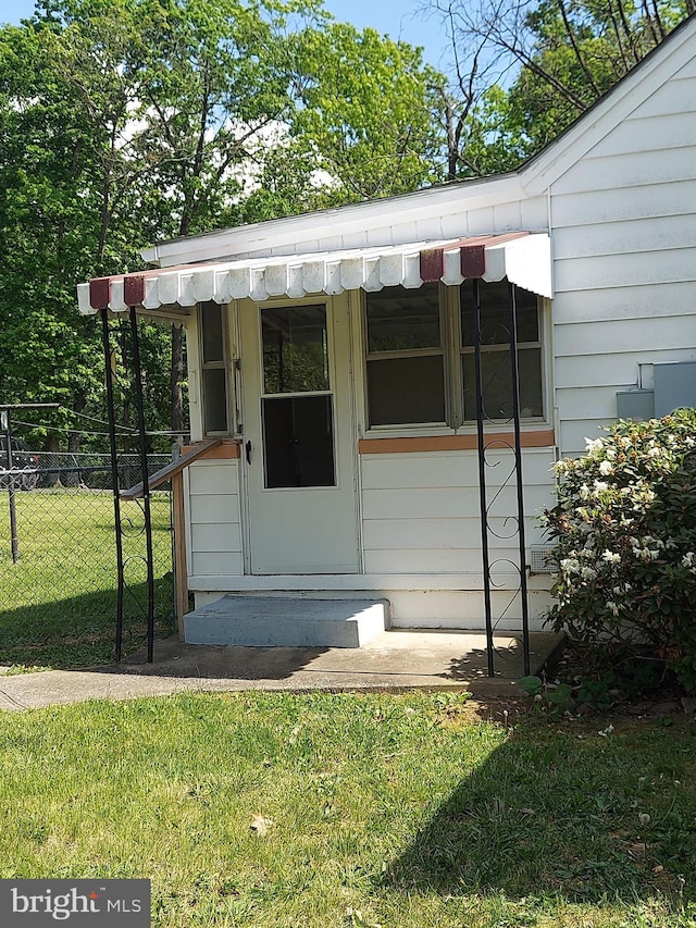 view of exterior entry with a lawn and fence
