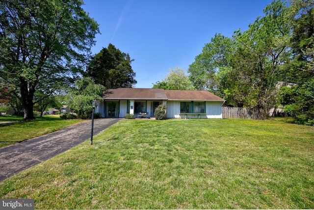 ranch-style home with a front lawn, aphalt driveway, fence, and covered porch