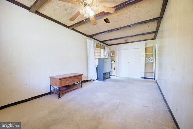 interior space featuring wooden walls, a ceiling fan, and beam ceiling