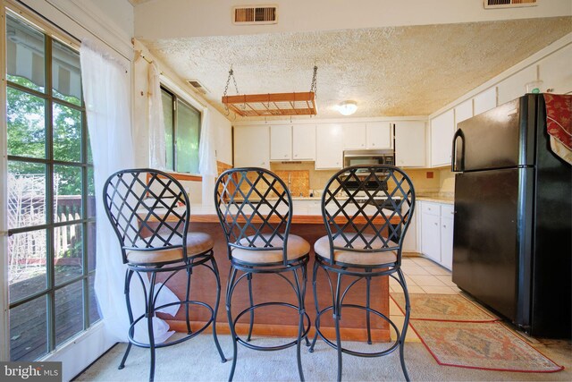 kitchen featuring visible vents, freestanding refrigerator, a peninsula, light countertops, and stainless steel microwave