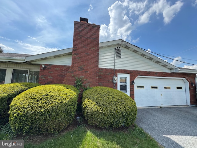 view of property exterior with a garage, a chimney, driveway, and brick siding
