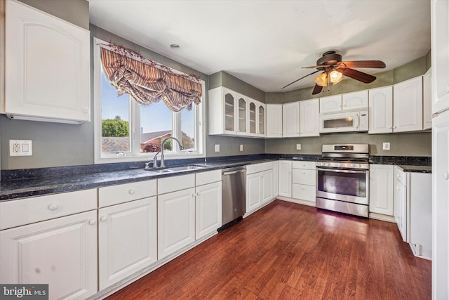 kitchen with a sink, dark wood finished floors, stainless steel appliances, white cabinetry, and glass insert cabinets