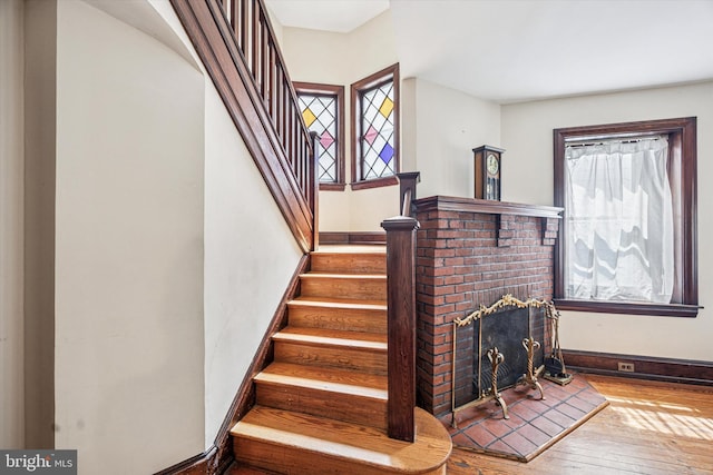 staircase featuring baseboards, wood-type flooring, and a brick fireplace