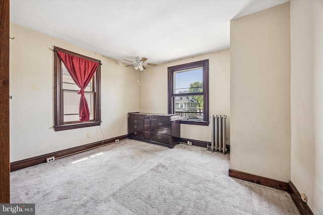 carpeted empty room featuring baseboards, a ceiling fan, and radiator