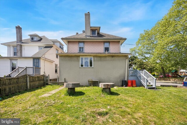 rear view of house featuring fence, stucco siding, a chimney, stairs, and a lawn