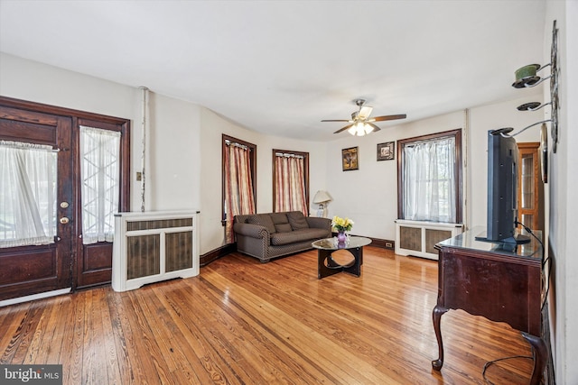 living area with wood-type flooring, ceiling fan, baseboards, and radiator heating unit