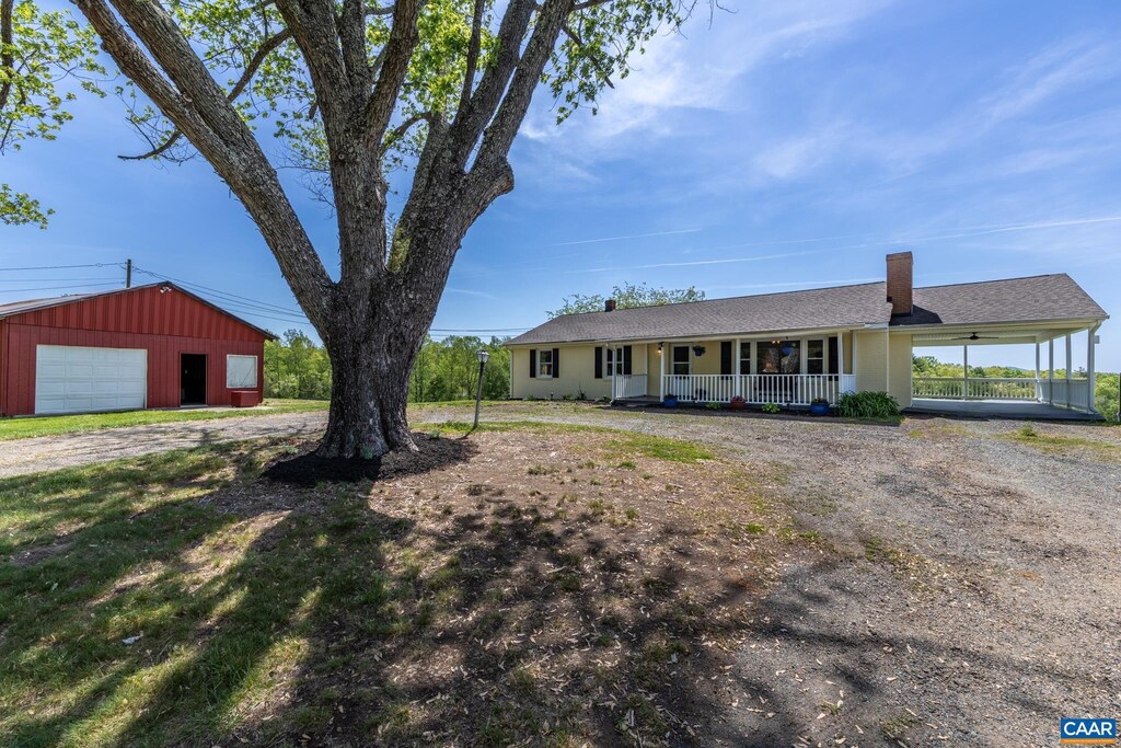 view of front of property featuring a garage, dirt driveway, a porch, a chimney, and an outdoor structure