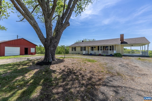 view of front of property featuring a garage, dirt driveway, a porch, a chimney, and an outdoor structure