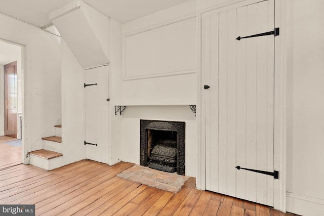 unfurnished living room featuring light wood-type flooring, a fireplace with flush hearth, and stairs