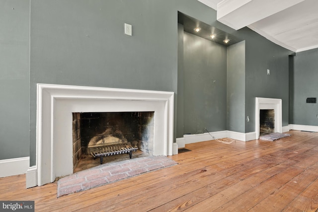 unfurnished living room featuring wood-type flooring, a fireplace with raised hearth, crown molding, and baseboards
