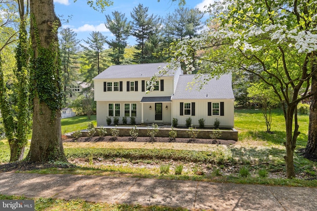 view of front of property featuring a front lawn, a patio area, and a shingled roof