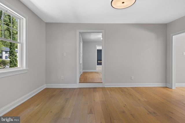 empty room with plenty of natural light, baseboards, and light wood-style floors