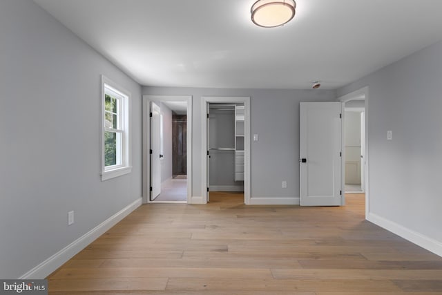 unfurnished bedroom featuring baseboards, a spacious closet, and light wood finished floors
