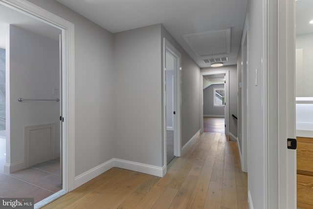 corridor with attic access, light wood-style floors, visible vents, and baseboards
