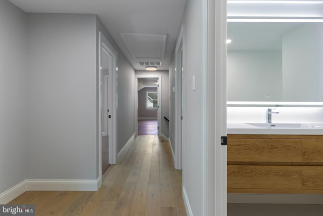 hall featuring a sink, attic access, visible vents, light wood finished floors, and baseboards