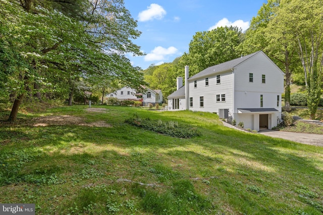 view of property exterior featuring a chimney, driveway, a yard, a garage, and central AC