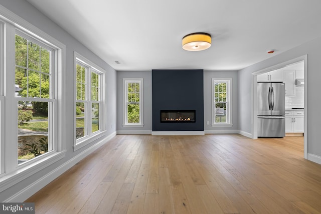 unfurnished living room with a wealth of natural light, baseboards, and light wood-type flooring