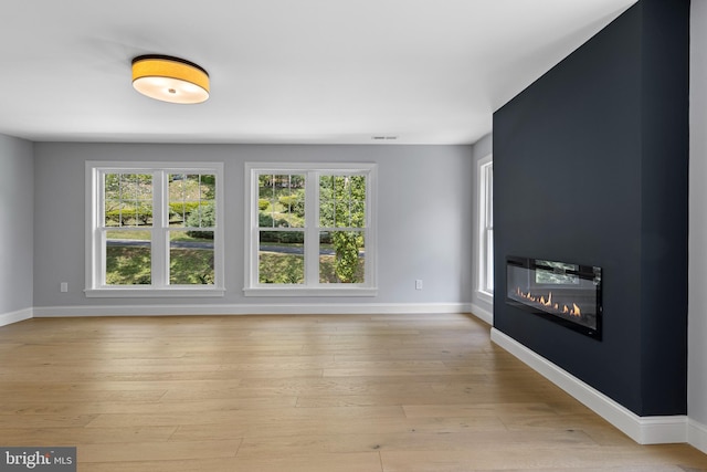 unfurnished living room with baseboards, light wood-type flooring, and a glass covered fireplace