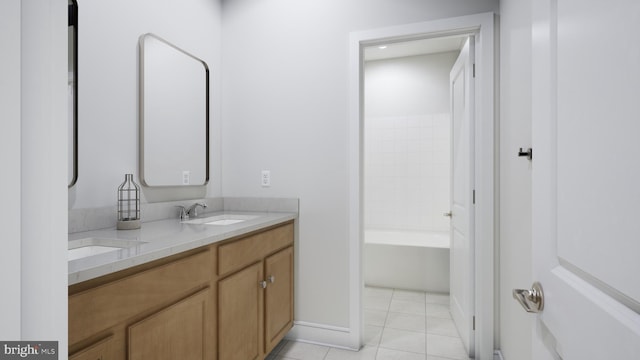 bathroom with a sink, double vanity, tile patterned floors, baseboards, and a bath