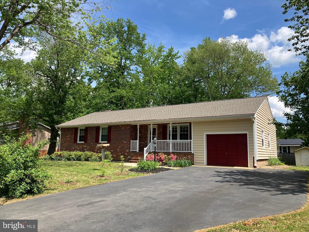 single story home featuring a garage, a porch, driveway, brick siding, and a front yard