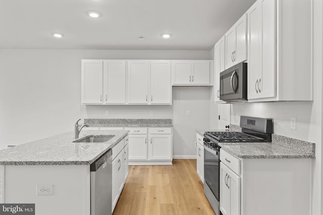 kitchen with light stone countertops, light wood-type flooring, white cabinetry, a sink, and stainless steel appliances