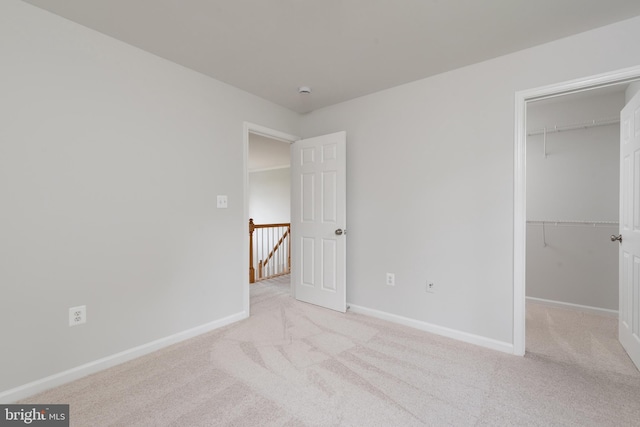 unfurnished bedroom with light colored carpet, a walk in closet, baseboards, and a closet