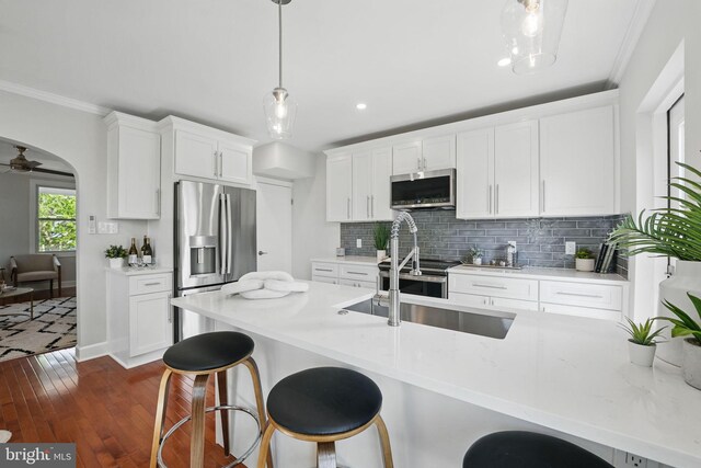 kitchen featuring appliances with stainless steel finishes, a sink, a kitchen bar, backsplash, and dark wood-style floors