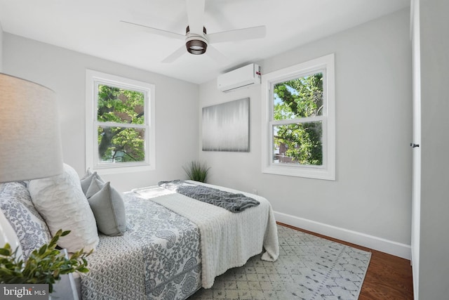 bedroom featuring baseboards, a wall unit AC, wood finished floors, and multiple windows