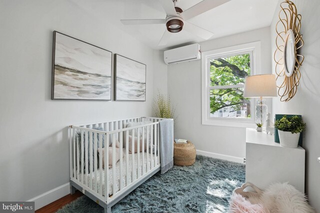 bedroom featuring a nursery area, baseboards, a ceiling fan, and a wall mounted air conditioner