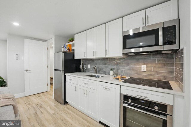 kitchen featuring appliances with stainless steel finishes, light wood-style flooring, a sink, light countertops, and white cabinetry